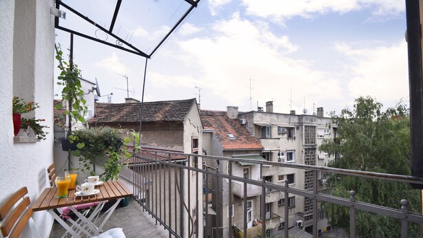A balcony with a table and chairs, a potted plant, and a view of surrounding buildings. - Apartment Tatjana (Zagreb)