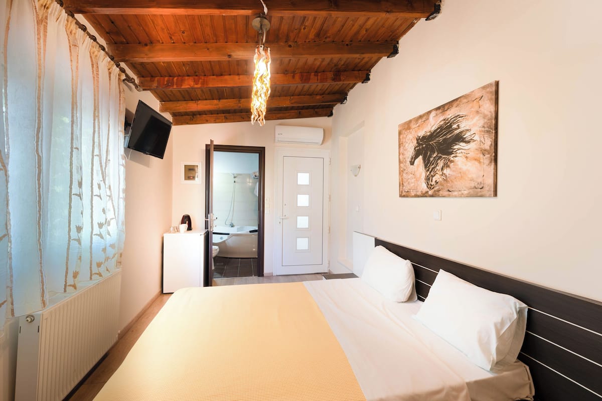 Ein Schlafzimmer mit Holzbalkendecke, einem Bett mit weißer Bettwäsche, einem an der Wand befestigten Fernseher und einem Bild.
