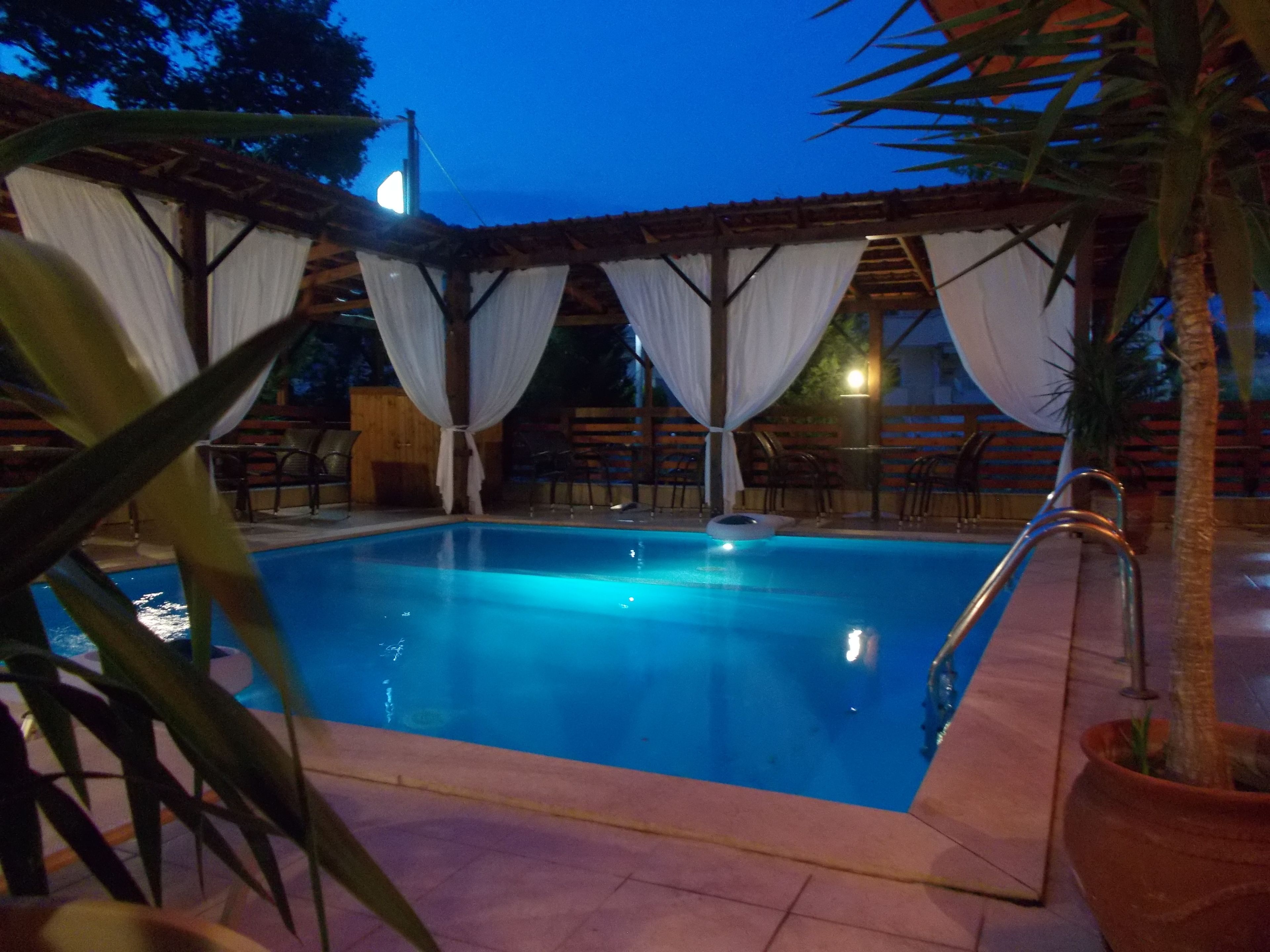 Una piscina con cubierta de madera y cortinas blancas.