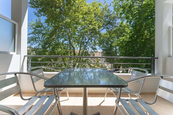 A balcony with a glass table and metal chairs, overlooking a tree-lined street. - Kipos Resort (Pangaio)