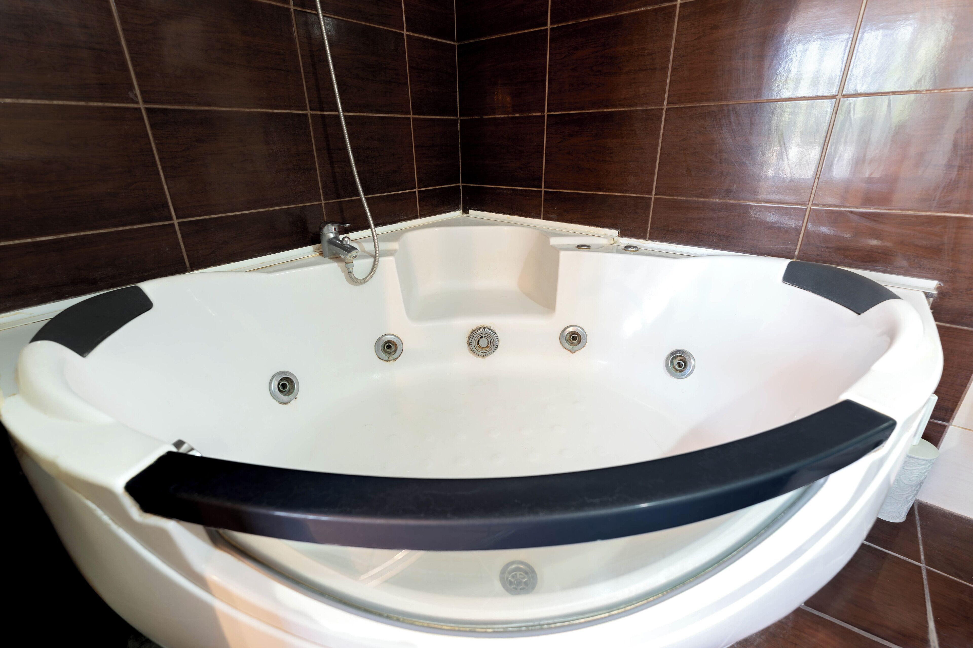 A white hot tub with a black rim, set against dark brown tiled walls.