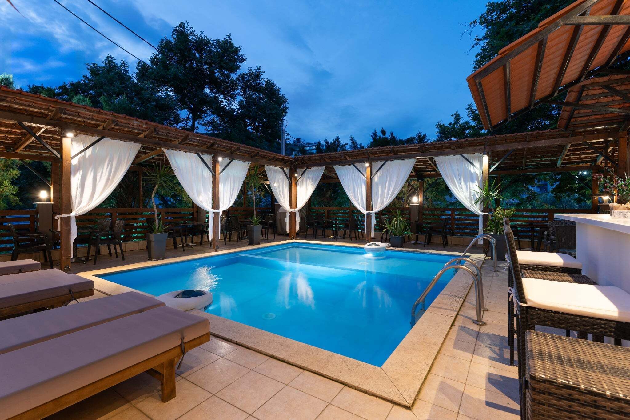 Una piscina con sillas de descanso y un área cubierta con cortinas blancas.