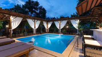 Una piscina con sillas de descanso y un área cubierta con cortinas blancas.