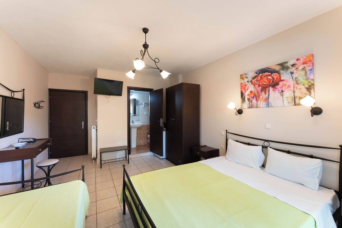 Ein Hotelzimmer mit Bett, Schreibtisch, Stuhl, Kleiderschrank und einem durch eine offene Tür einsehbaren Badezimmer.