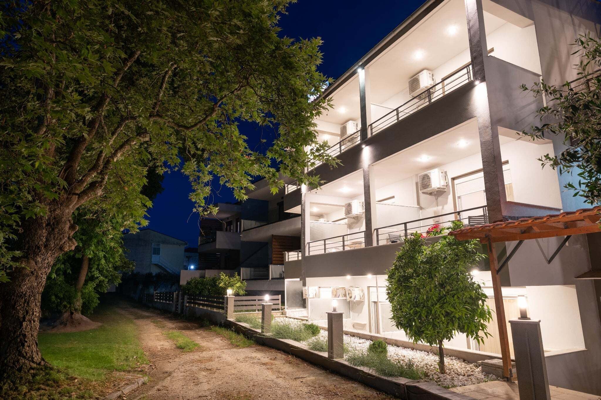 Un edificio de varios pisos con balcones, iluminación exterior y un camino que lleva a la entrada.