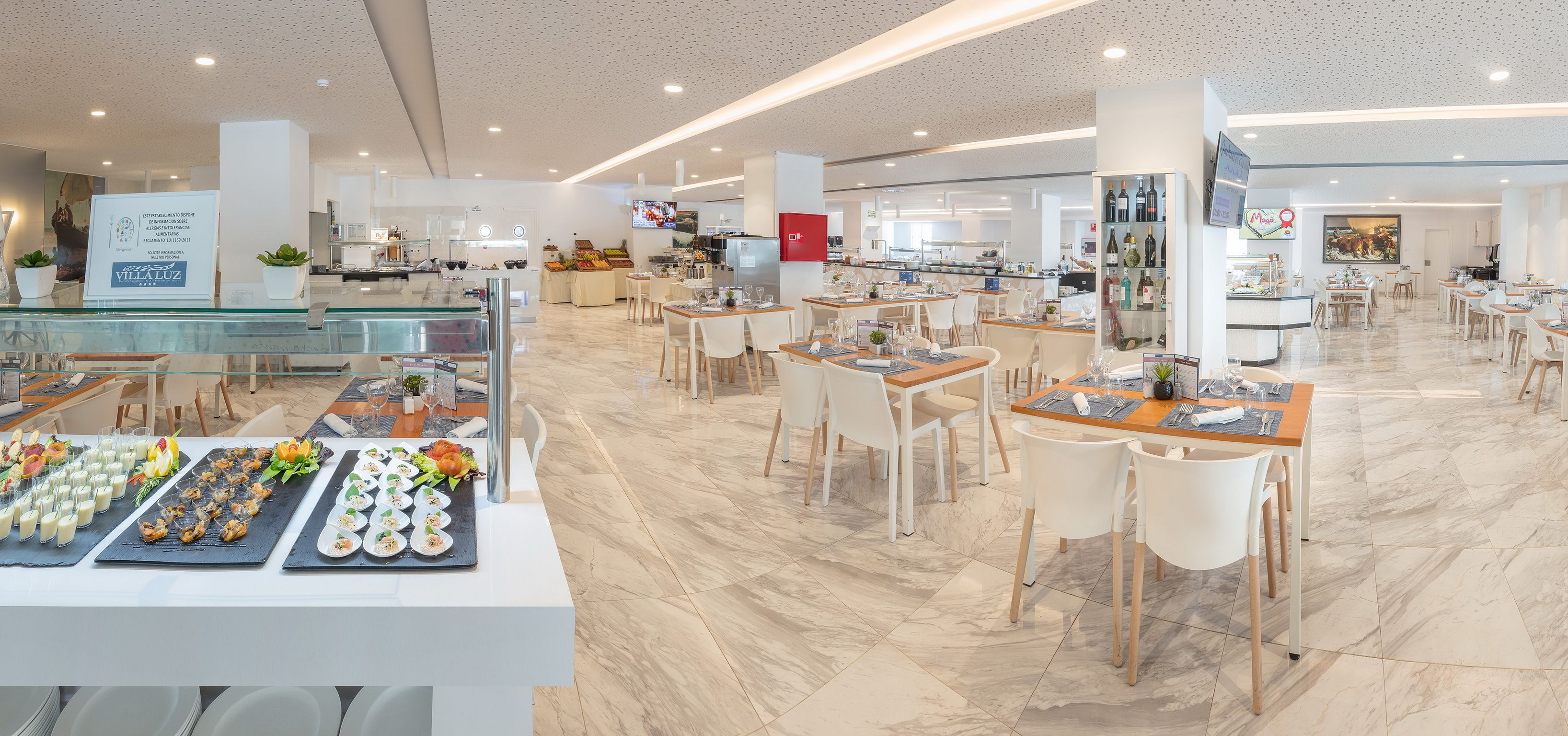Un hall d’hôtel spacieux comprenant plusieurs espaces de restauration, un comptoir d’accueil et une cuisine en arrière-plan.