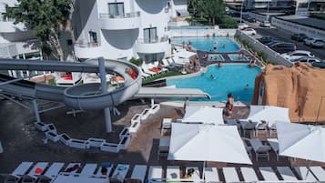 Un hotel con una amplia zona de piscina, que incluye un tobogán acuático y varias áreas de descanso con sombrillas.