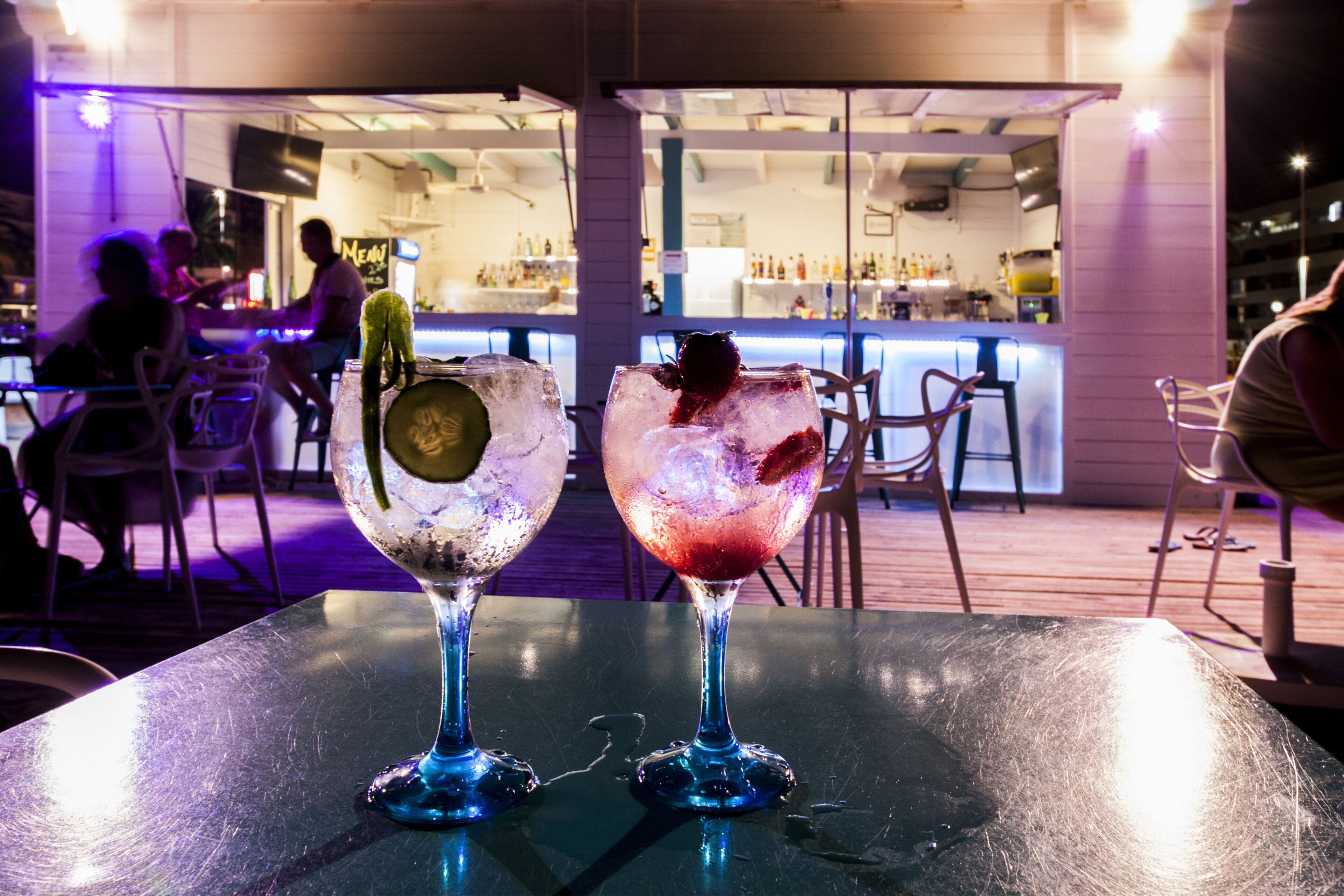 Two drinks on a table with a bar in the background.