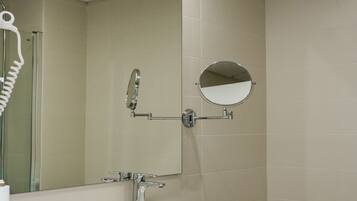 Un baño moderno con un lavamanos blanco, un espejo redondo, cabina de ducha de vidrio y un bidé.