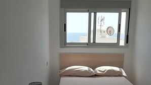 Un dormitorio con cama, una mesita de noche con lámpara, una ventana con vista al mar y una luz en el techo.