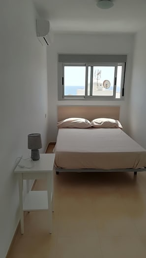 Un dormitorio con cama, una mesita de noche con lámpara, una ventana con vista al mar y una luz en el techo.