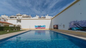 Une piscine à l’eau d’un bleu cristallin, entourée de murs blancs et ornée d’une fresque représentant des palmiers et un coucher de soleil.