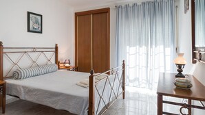 Une chambre à coucher avec un lit en bois, une table de chevet, une lampe, une armoire et une fenêtre avec des rideaux.