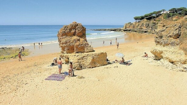 Une plage avec des formations rocheuses, des gens qui prennent un bain de soleil et un ciel dégagé.