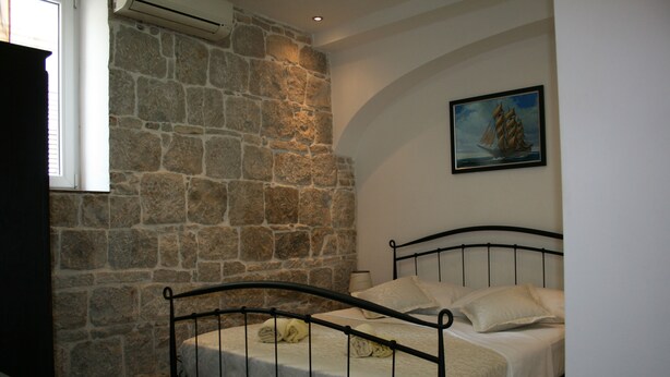Quarto com parede de pedra, cama com estrutura de metal e pintura de um navio na parede.