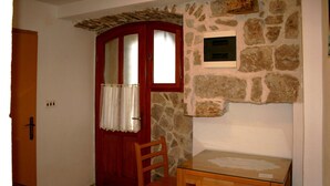 Um quarto com parede de pedra, porta de madeira com painéis de vidro, uma pequena mesa e uma cadeira.