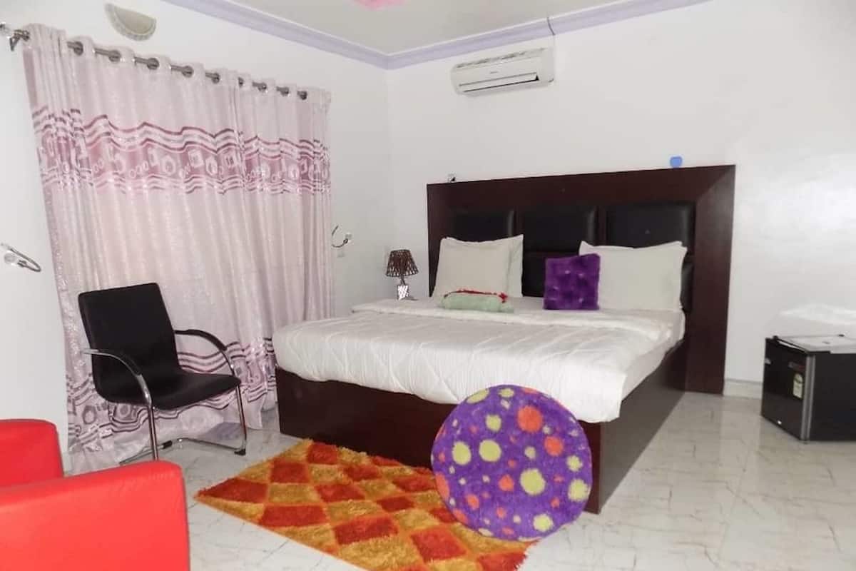 Ein Schlafzimmer mit einem Bett, einem Sessel, einem kleinen Tisch, einem Heizgerät und einem Fenster mit Vorhängen.