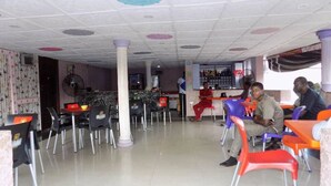 A restaurant with a tiled floor, multiple tables and chairs, and a bar area in the background. - De Fellas Palace Hotel & Suites (Ibadan)