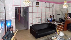 A reception area with a black leather sofa, a reception desk, and a person seated at a desk. - De Fellas Palace Hotel & Suites (Ibadan)
