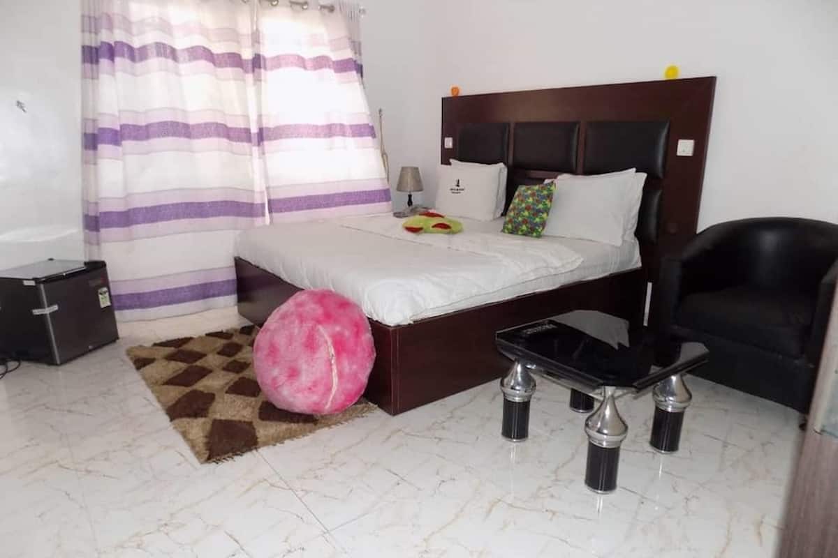 Ein Schlafzimmer mit Bett, Schreibtisch, Stuhl, Hocker in Rosa, Lampe und Koffer.