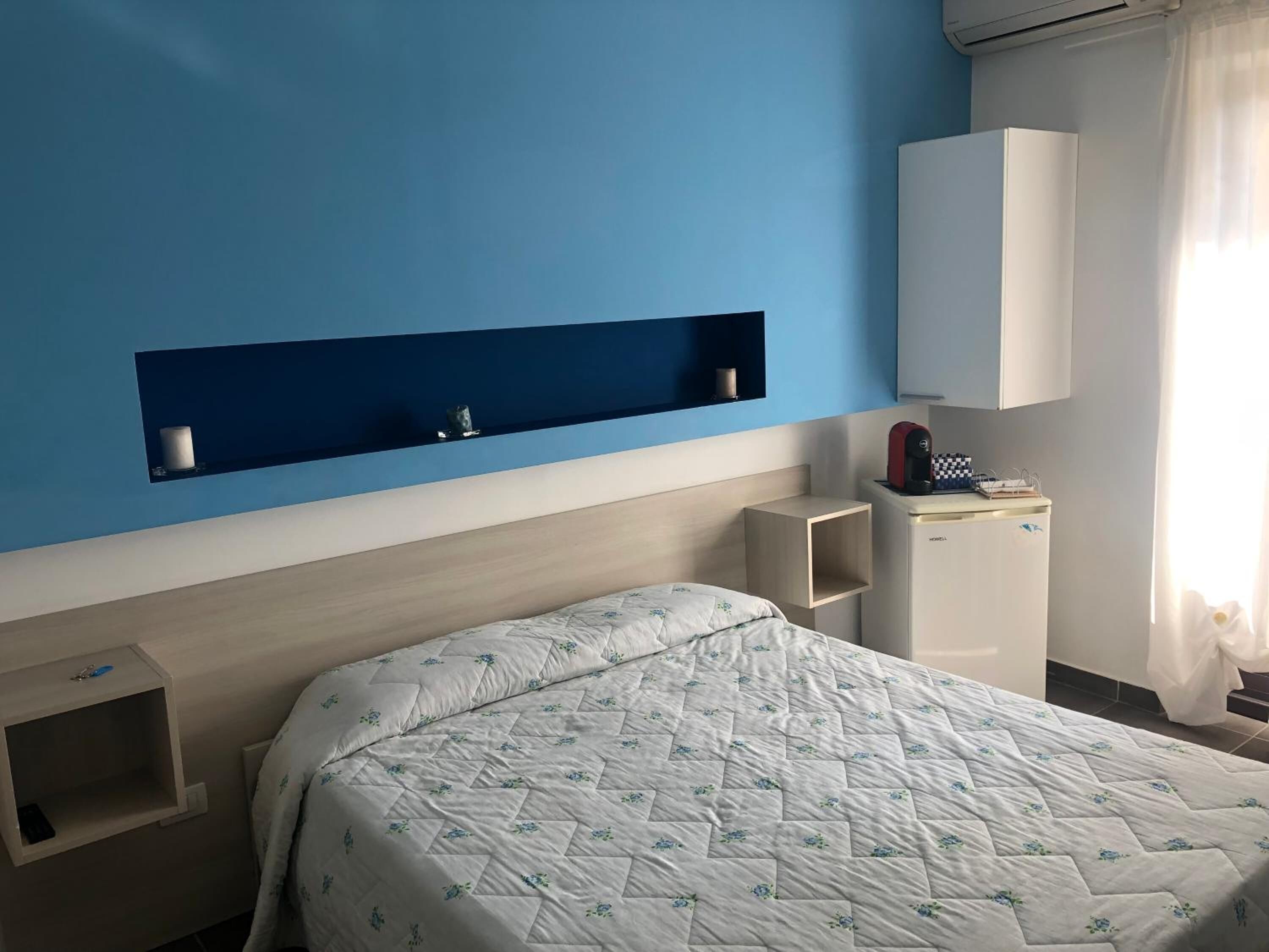 A hotel room with a bed, a small bedside table, a built-in shelf, and a wardrobe.