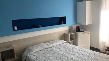 A hotel room with a bed, a small bedside table, a built-in shelf, and a wardrobe.