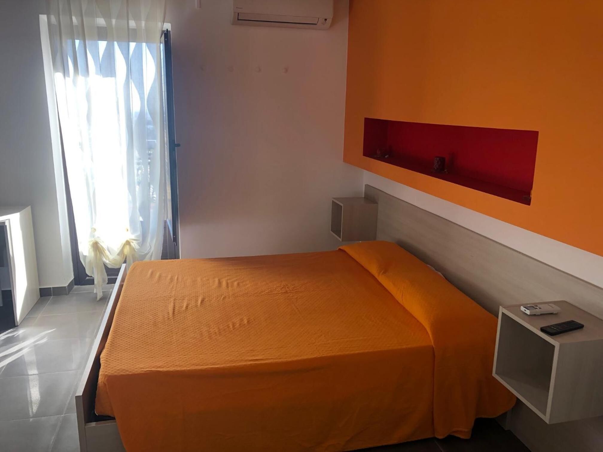 A hotel room with a bed, a nightstand, and a red accent wall.