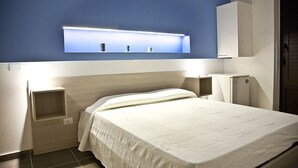 Una habitación de hotel con cama, mesitas de noche, un estante en la pared con objetos decorativos y un armario.