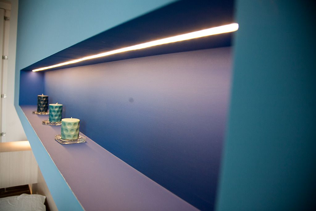 A hallway with a blue wall and a white floor, featuring three teal-colored candles on a shelf.