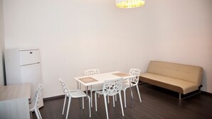 Una habitación moderna con una mesa de comedor, sillas blancas, un sofá color crema y un refrigerador blanco.