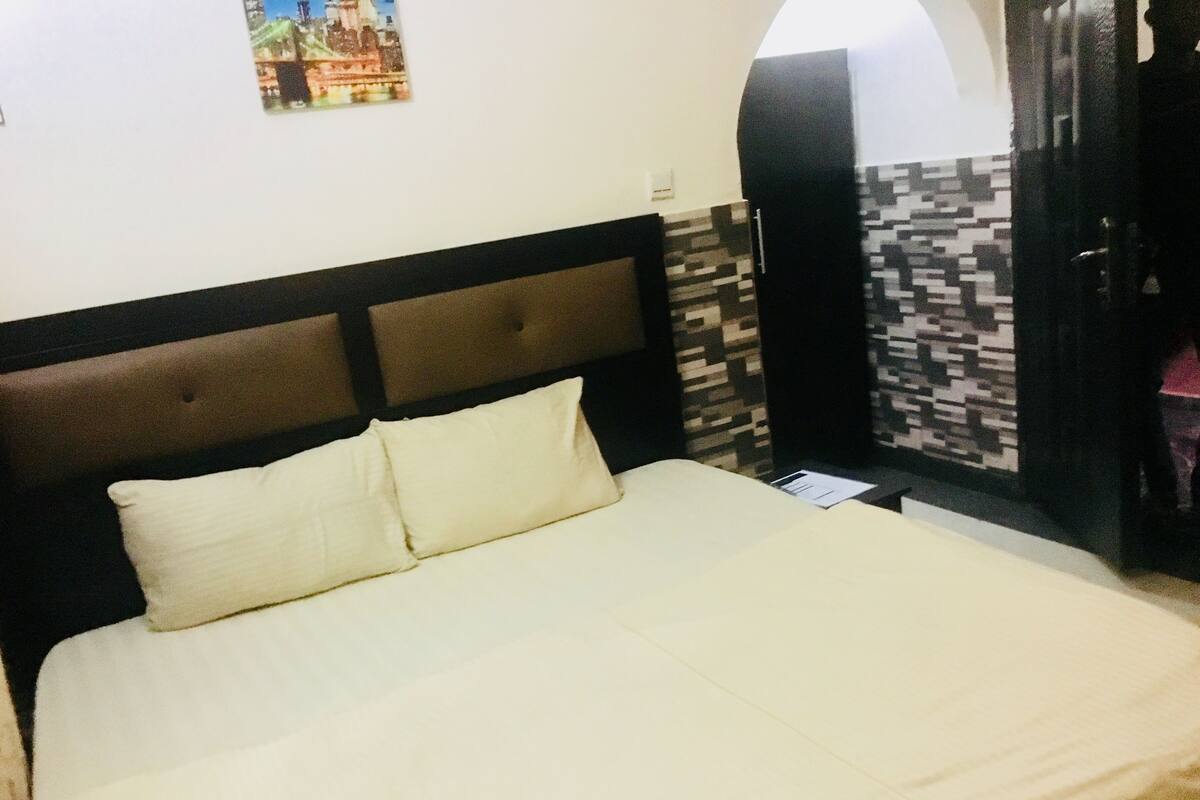 Una cama con cabecera, un almohadón y un cuadro colgado en la pared.