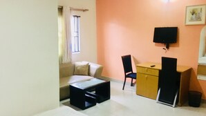 Uma sala de estar com sofá, mesa de centro, TV fixada na parede e escrivaninha com cadeira.
