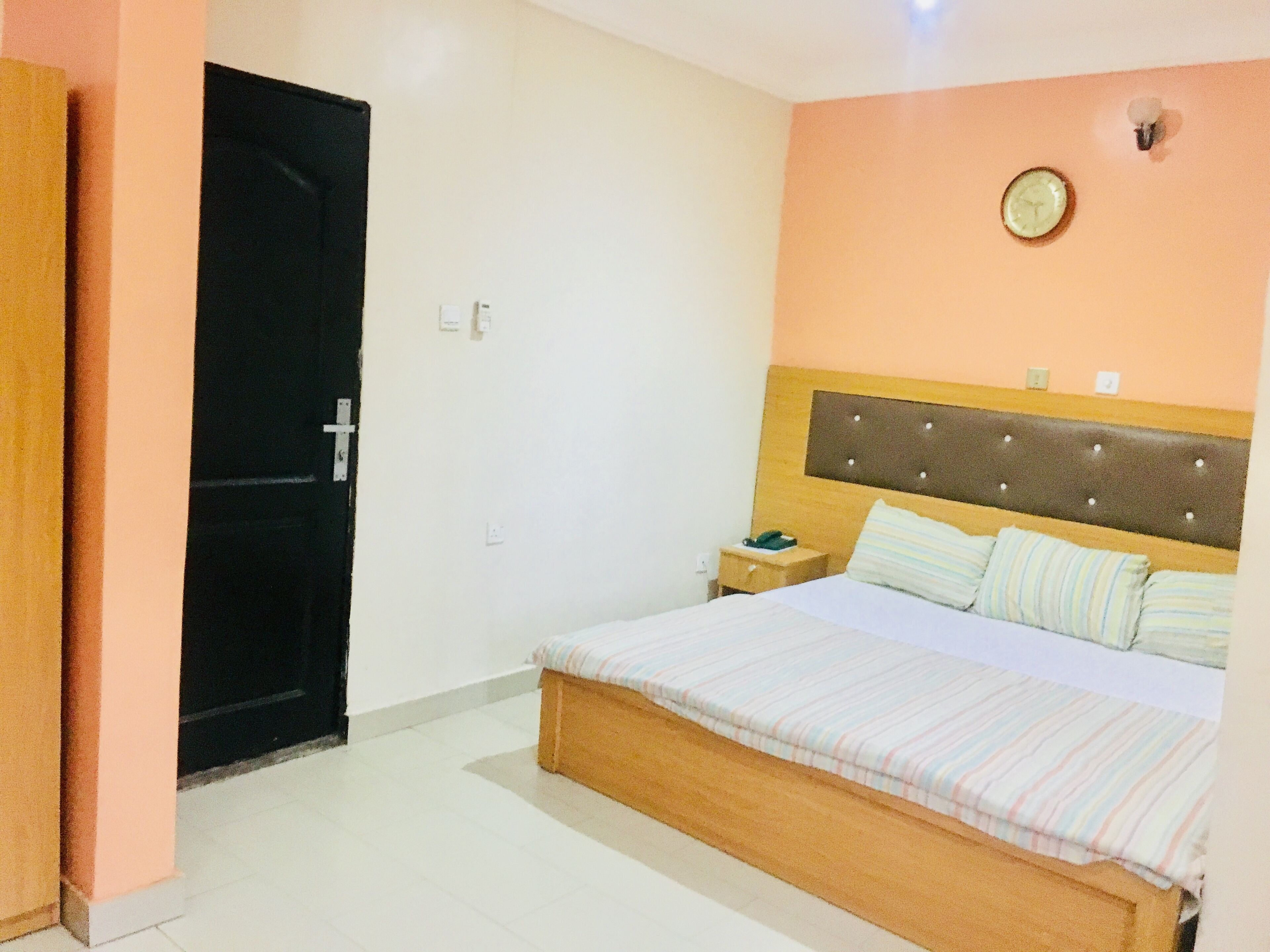 A bedroom with a bed, a nightstand, a wall clock, and a door.