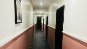 Um corredor comprido e estreito, com piso preto, paredes brancas e rodapé vermelho.
