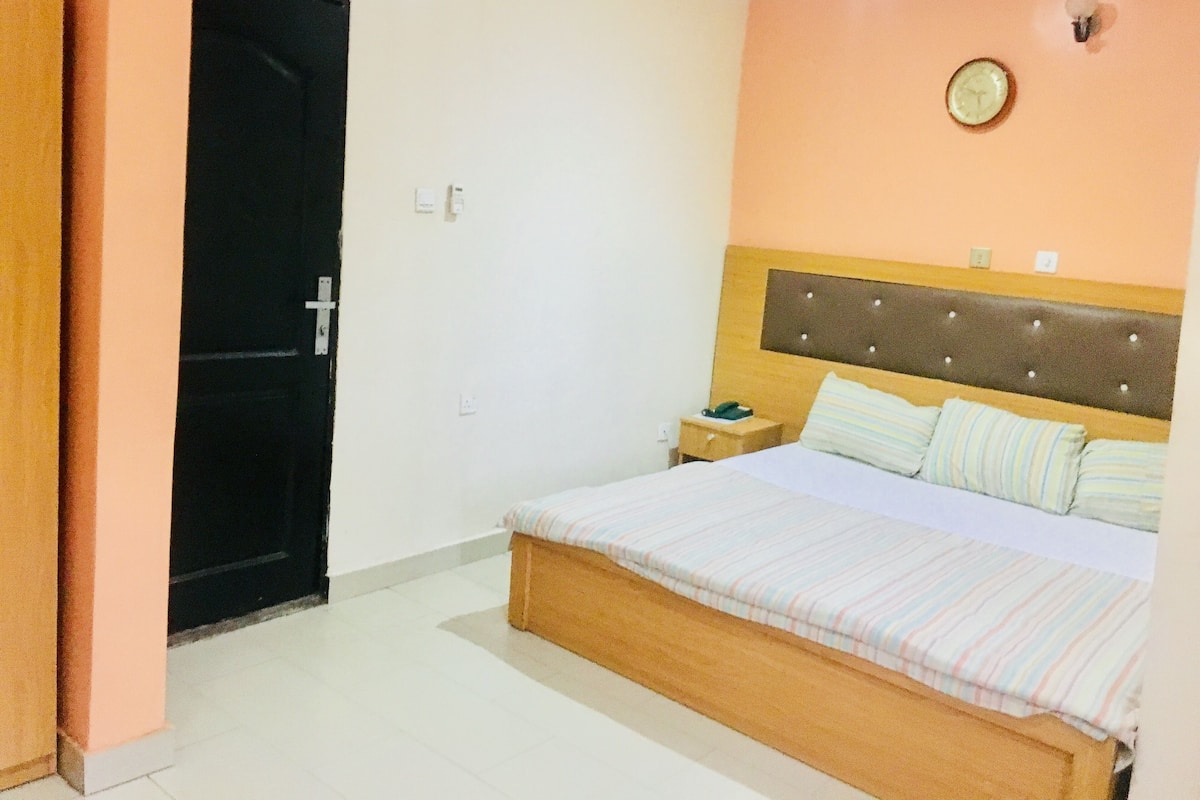 Un dormitorio con una cama, una mesita de noche, un reloj de pared y una puerta.