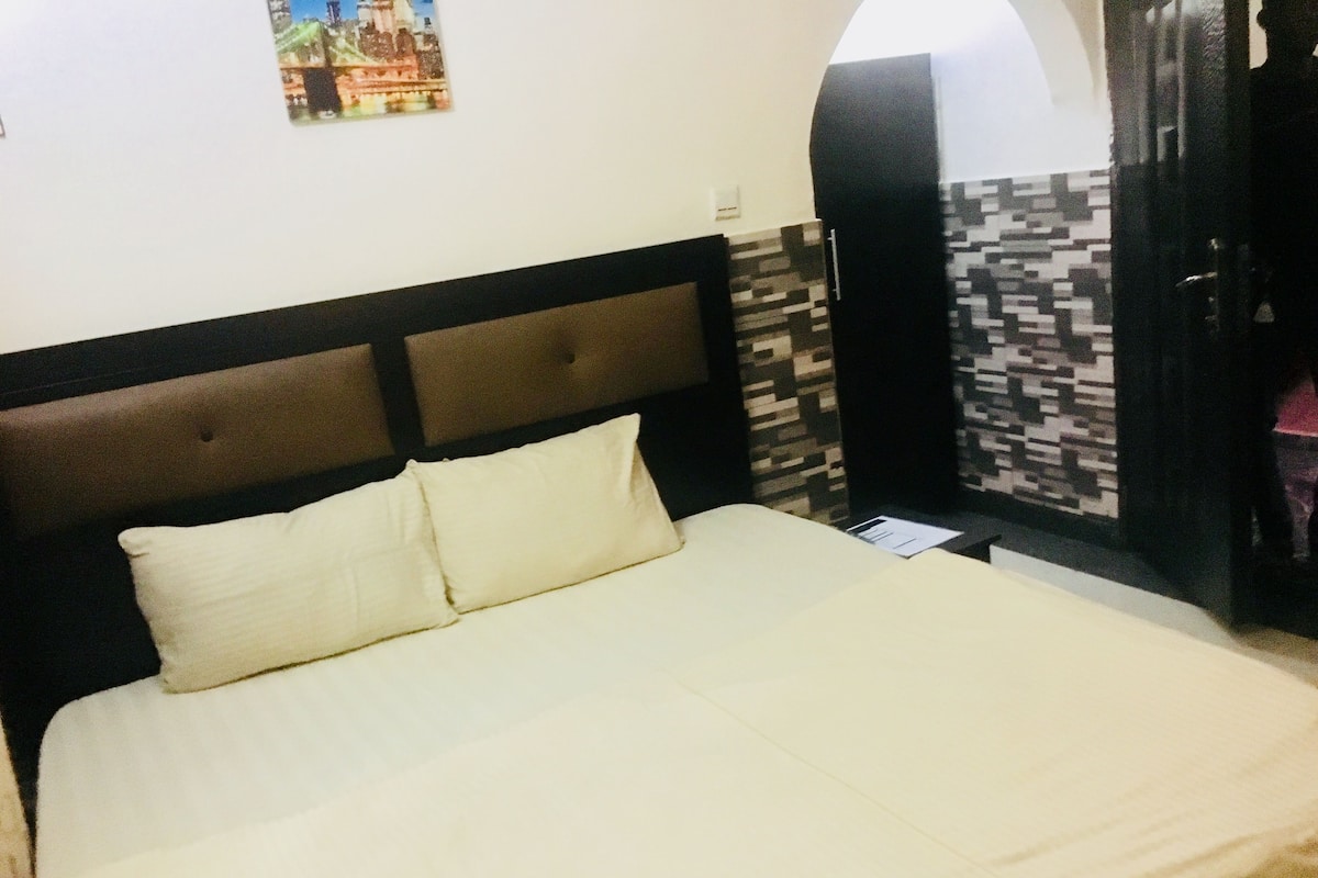 Una cama con cabecera, un almohadón y un cuadro colgado en la pared.