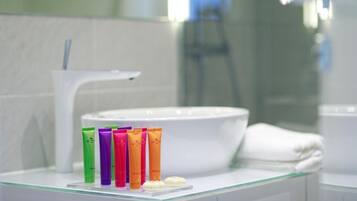 Een badkamer met een wit wastafel, een glazen aanrechtblad en een rij kleurrijke toiletartikelen.