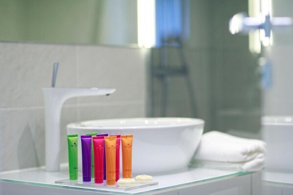 A bathroom with a white sink, a glass countertop, and a row of colorful toiletries. - Hotel 9 (Zagreb)