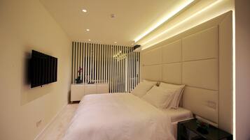 Un dormitorio moderno con una cama grande, un televisor montado en la pared y una mesita de noche con una lámpara.