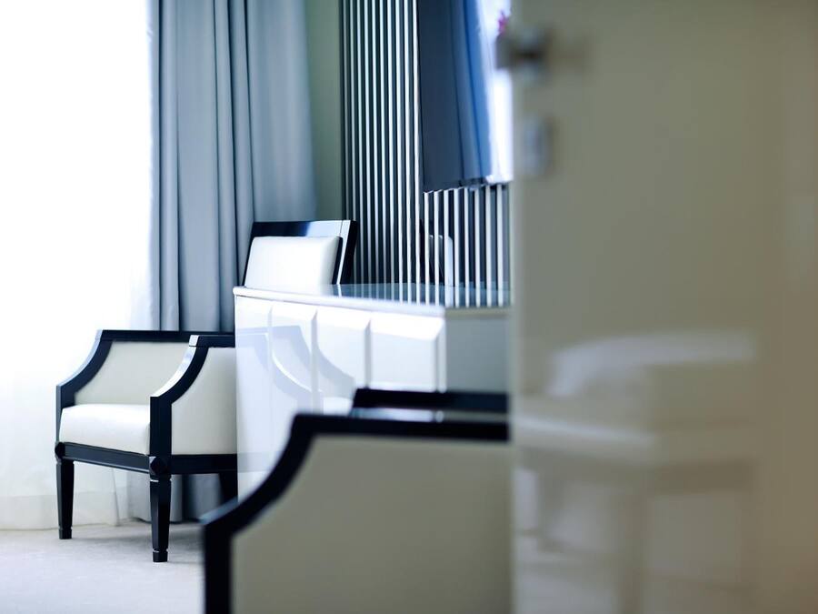 Una habitación de hotel moderna con un sofá blanco, un sillón con marco negro y un aparador blanco.