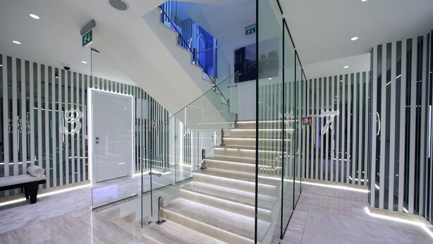 Un hall d’hôtel moderne avec un escalier en verre, un sol en marbre et des murs à rayures.