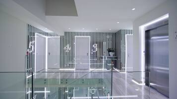 Um hall de hotel moderno com guarda-corpos de vidro, uma escadaria e um elevador de aço inoxidável.