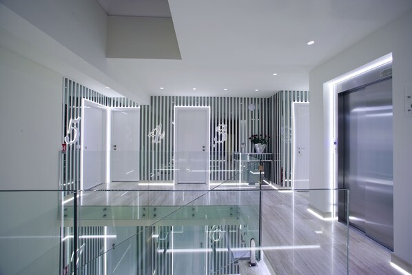 Un hall d’hôtel moderne avec des rampes en verre, un escalier et un ascenseur en acier inoxydable.