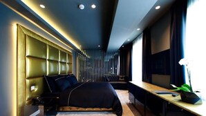 Une chambre à coucher moderne avec une tête de lit capitonnée, un lit, un bureau et une grande fenêtre.