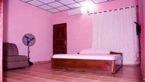 Een kamer met roze muren, een bed, een ventilator en een gestreept bankje.