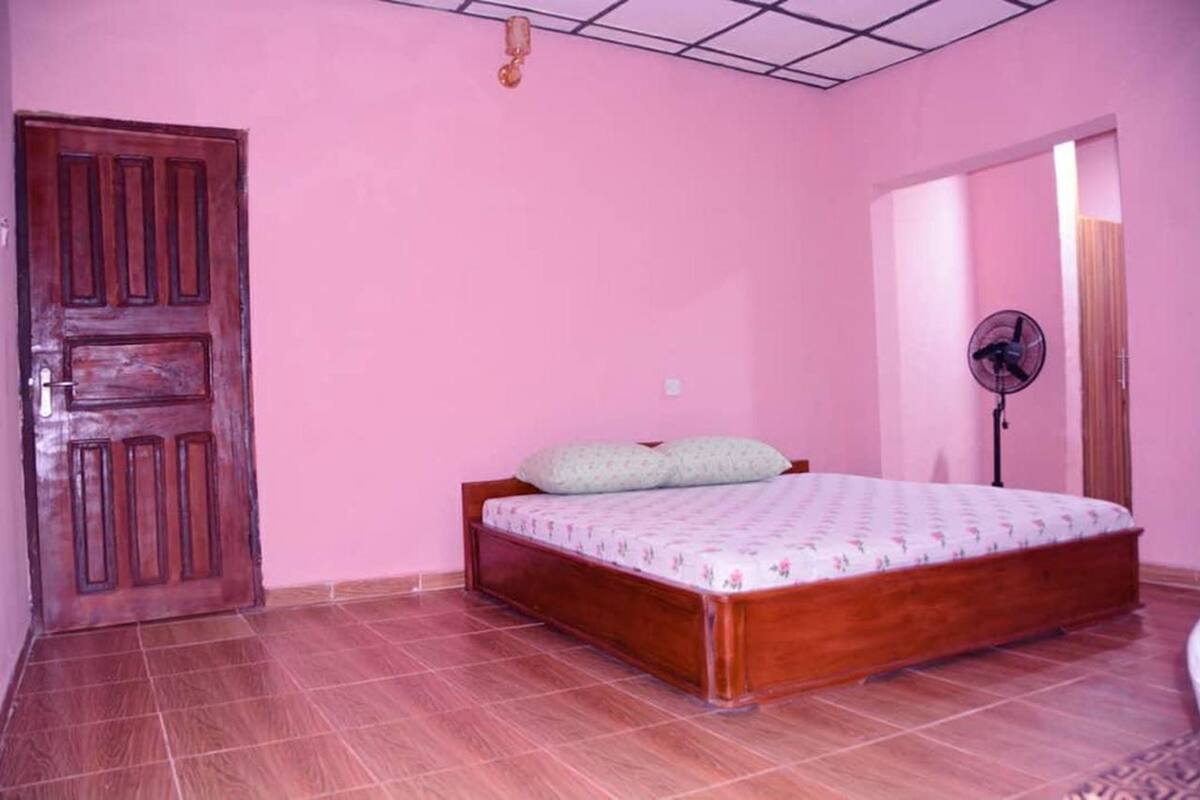 A bedroom with a wooden bed, a pink wall, a tiled floor, and a door.