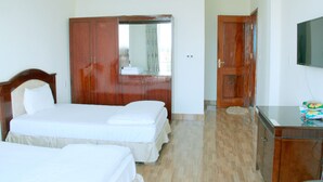 A hotel room with two beds, a wardrobe, a mirror, and a television.