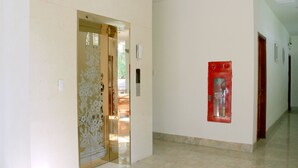 A hallway with a door leading to a room, a fire extinguisher mounted on the wall, and a tiled floor.