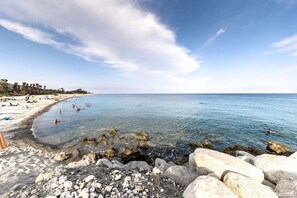 A beach with clear water, rocky shore, and people swimming. - Villaggio Camping Calypso (Caulonia)