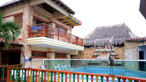 Un edificio de dos plantas con un balcón, una estructura de techo de paja y una piscina.